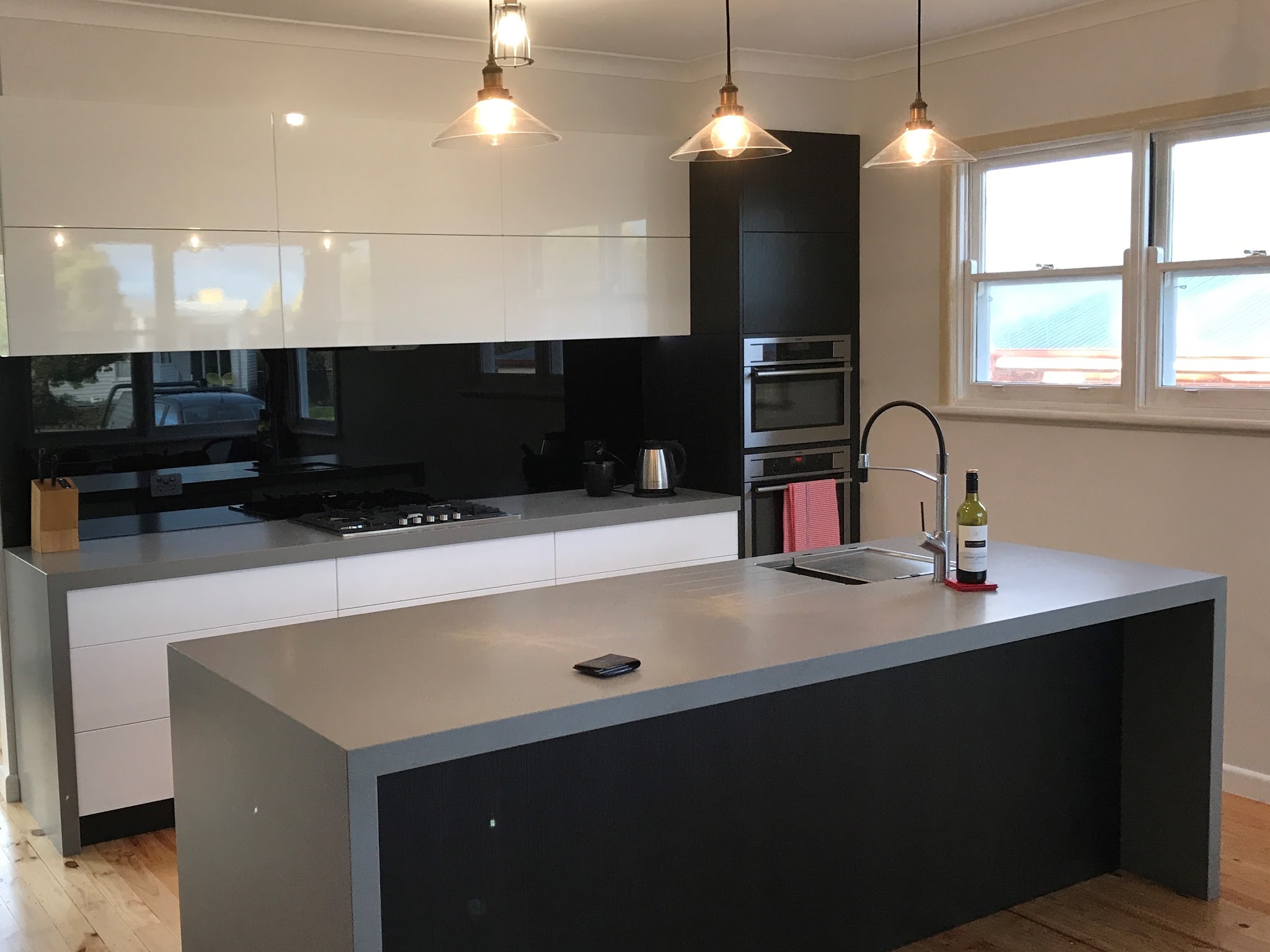 Modern kitchen with gloss white overheads, a black glass splashback and a stone island