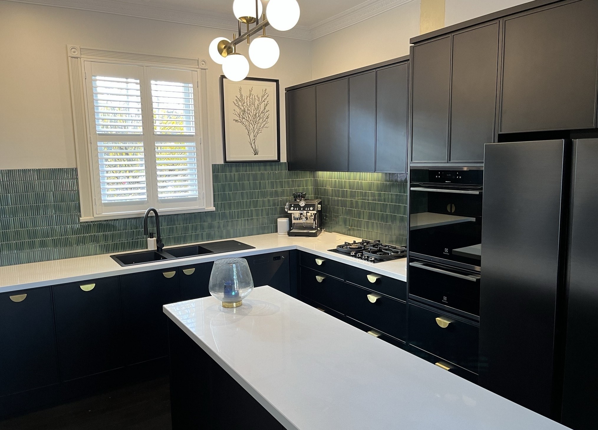 Navy kitchen with a green tile splashback and brass half moon handles